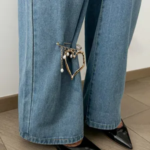 Macro view of a golden lava heart brooch with pearls and chain tassels on jeans