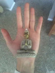 Detailed macro view of a mini Southeast Asian Buddha statue held in a palm for size reference