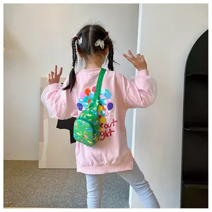 Close-up detail of the green cartoon dinosaur chest bag worn by a child on a pink shirt