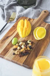 Solid acacia wood serving board with handle displaying sliced mango and mixed nuts