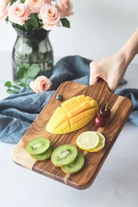 Detail of natural acacia wood serving board with handle holding sliced fruits
