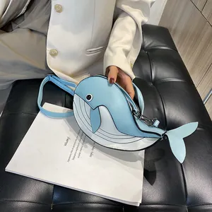 Detail shot of a cute light blue cartoon whale-shaped crossbody bag on a leather sofa.