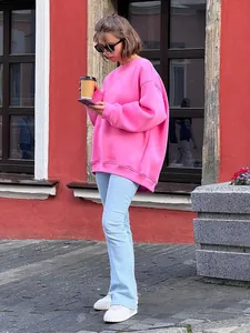 Woman in oversized bright pink pullover sweatshirt and light blue jeans on city street