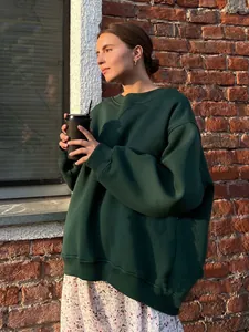 Detail of an oversized dark green crewneck sweatshirt in an outdoor lifestyle setting