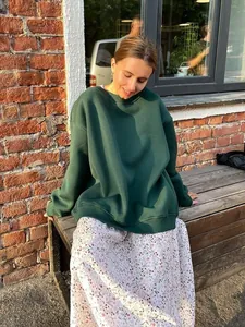 Stylish woman wearing a dark green oversized sweatshirt sitting on a wooden bench outdoors.