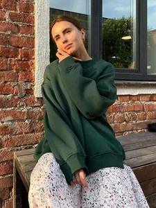 Detail view of a dark green oversized crewneck fleece sweatshirt worn outdoors