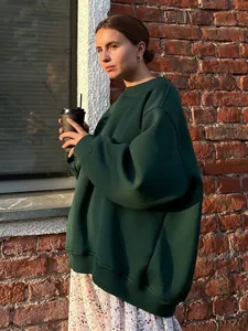 Side view of woman wearing an oversized dark green crewneck sweatshirt in urban setting