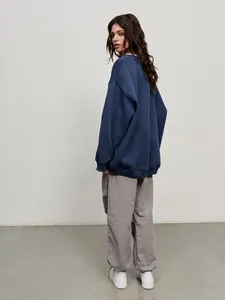 Rear view of a model wearing an oversized blue crew neck sweatshirt with grey pants