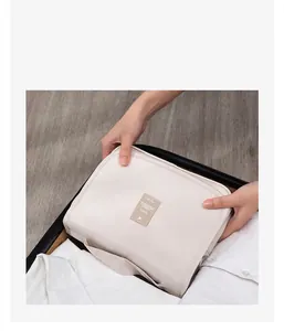 Detail view of a beige waterproof toiletry bag being placed into a travel suitcase.