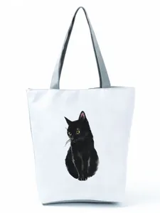 Close-up detail of white canvas tote bag featuring a minimalist black cat illustration print.