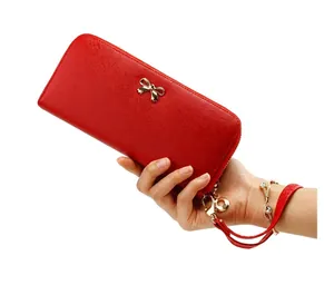 Cartera larga de cuero PU rojo con lazo dorado sostenida en la mano fondo blanco