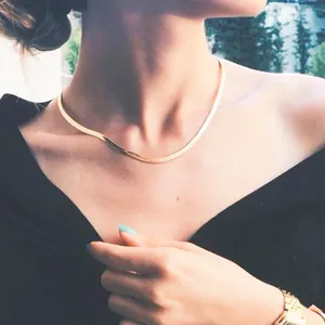 Close-up detail of an elegant gold herringbone snake chain necklace worn by a woman