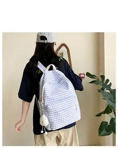 Close-up of a blue gingham backpack with a white bow and plush charm on a model