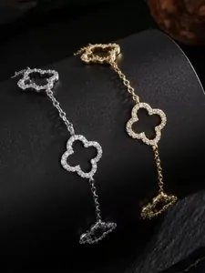 Primo piano di bracciali a quadrifoglio in oro e argento con pavé di pietre lucenti.