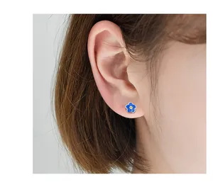 Detailed view of a small blue flower earring in s925 silver on a human ear lobe