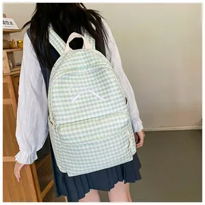 Close-up of green and white checkered school backpack with white bow detail on model.