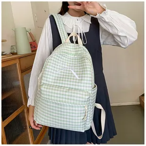 Lifestyle view of a green checkered backpack with a white bow embroidery worn by a student