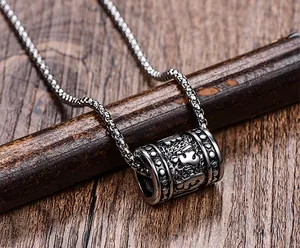 Gros plan détaillé du pendentif cylindre en acier inoxydable aux motifs sanskrits.
