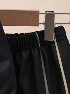 Macro shot of black joggers waistband showing elastic detail and gold side stripes