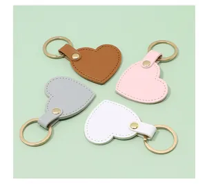 Top view of four heart-shaped leather keychains in brown, pink, grey, and white colors.