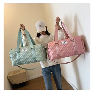 Model holding two quilted travel duffel bags in mint green and pink colors