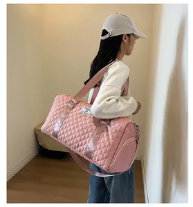 Detail view of large pink quilted travel duffle bag worn by female model in white cap