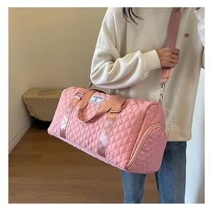 Detail view of a lightweight pink quilted duffel bag carried by a model for travel use.