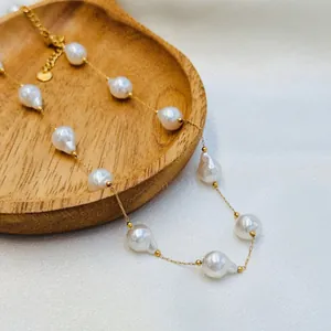 Close-up of elegant baroque pearl necklace with thin gold chain on wooden tray