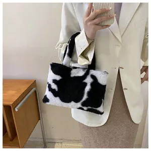Detailed view of a stylish black and white cow print plush handbag held by a model.