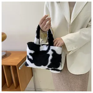 Detailed shot of a stylish black and white cow print plush handbag held by a model.