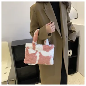 Close-up of pink and white plush cow-print handbag held by a model in a coat