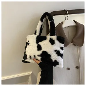 Close-up view of a stylish small plush handbag with black and white cow print held by hand