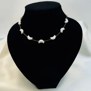 Detailed close-up of a gold necklace with white shell crescent pendants on a black bust