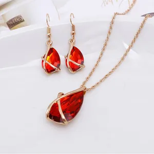Close-up of teardrop red gemstone jewelry set with hollow gold-tone cross frame.