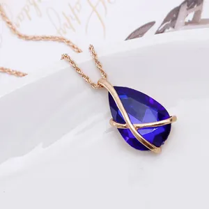 Close-up of teardrop blue gemstone necklace with elegant gold cross frame setting