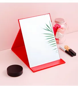 Detail view of a red folding makeup mirror with premium leather stand on a soft pink background.