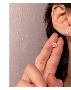 Close-up view of S999 silver stud earring with sparkling zircon on ear and finger.