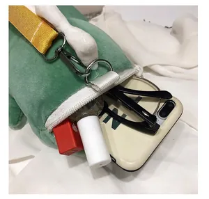Close-up of green plush dinosaur bag showing capacity for phone and glasses