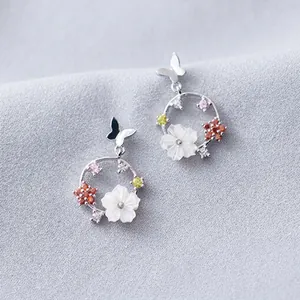 Detailed view of silver earrings with floral and butterfly motifs and colorful stones.