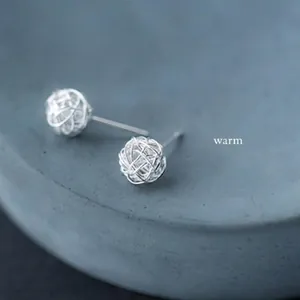 Close-up of S925 silver woven wire ball stud earrings on a minimalist grey stone base