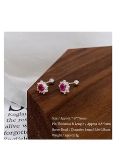 Close-up of S999 silver snowflake stud earrings with vibrant red zircon on wood