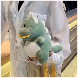 Cute green plush dinosaur crossbody bag held by a person in a white shirt indoors