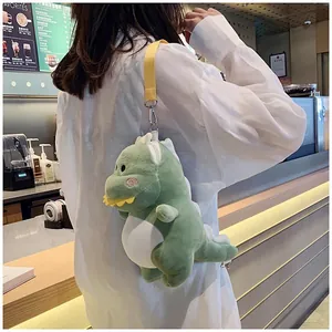 Plush green dinosaur crossbody bag worn by a model in a cozy cafe lifestyle setting