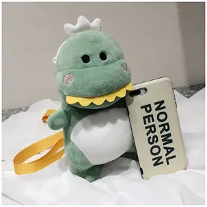 Close-up of a cute green dinosaur plush crossbody bag next to a smartphone for size reference