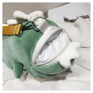 Close-up of green plush dinosaur crossbody bag with yellow strap and zipper opening.