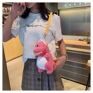Close-up of a cute pink dinosaur plush crossbody bag worn by a person in white.