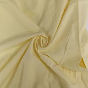Close-up detail of high-quality soft pale yellow dress fabric showing smooth texture and drape