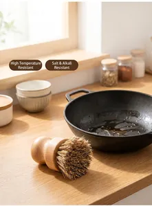 Close-up of a beech wood kitchen brush with natural sisal bristles near a cast iron pan.