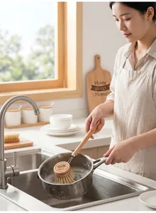 Detailed view of a long-handled wooden dish brush washing a pot in a kitchen sink.