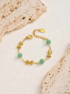 Macro detail of a gold stainless steel bracelet with green beads and bow charms decoration.